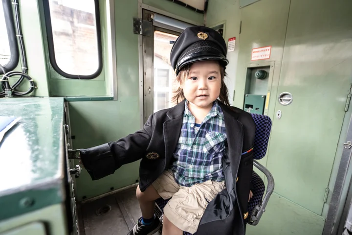 JR九州の制服と制帽を着用し、キハ40形車両の前で誇らしげにポーズをとる子ども