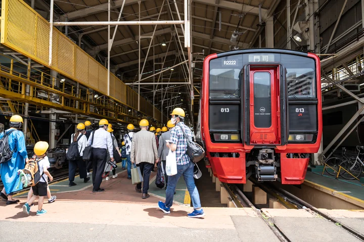 巨大なクレーンや整備中の813系車両が並ぶ、小倉総合車両センターの工場内部