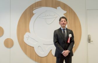 シャボン玉石けんの新研究拠点「イノベーションラボ北九州」開所式にて、同社ロゴを背景に立つ森田隼人代表取締役社長。
