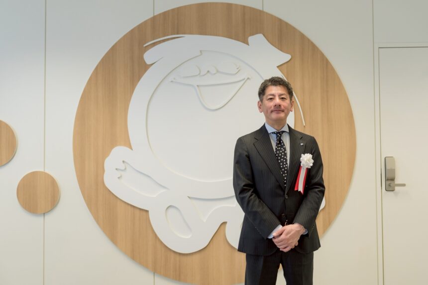 シャボン玉石けんの新研究拠点「イノベーションラボ北九州」開所式にて、同社ロゴを背景に立つ森田隼人代表取締役社長。